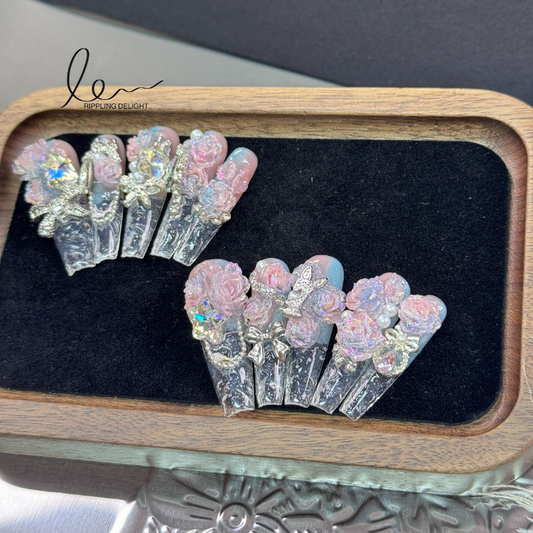 （Long-Length Coffin）The handmade nail tips have a transparent - to - pink base, with lifelike pink roses, shiny rhinestones, and bows.