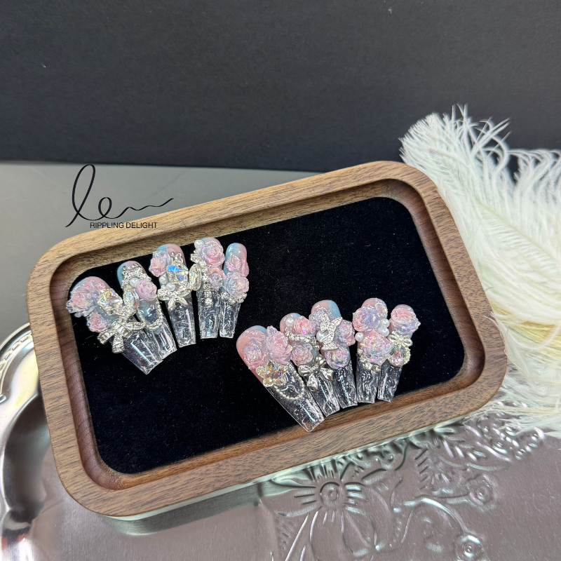 （Long-Length Coffin）The handmade nail tips have a transparent - to - pink base, with lifelike pink roses, shiny rhinestones, and bows.