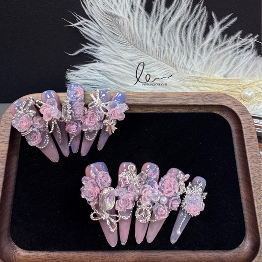 Handmade nail tips feature lifelike pink flowers, encircled by sparkling rhinestones and silver chains.