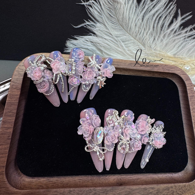 Handmade nail tips feature lifelike pink flowers, encircled by sparkling rhinestones and silver chains.