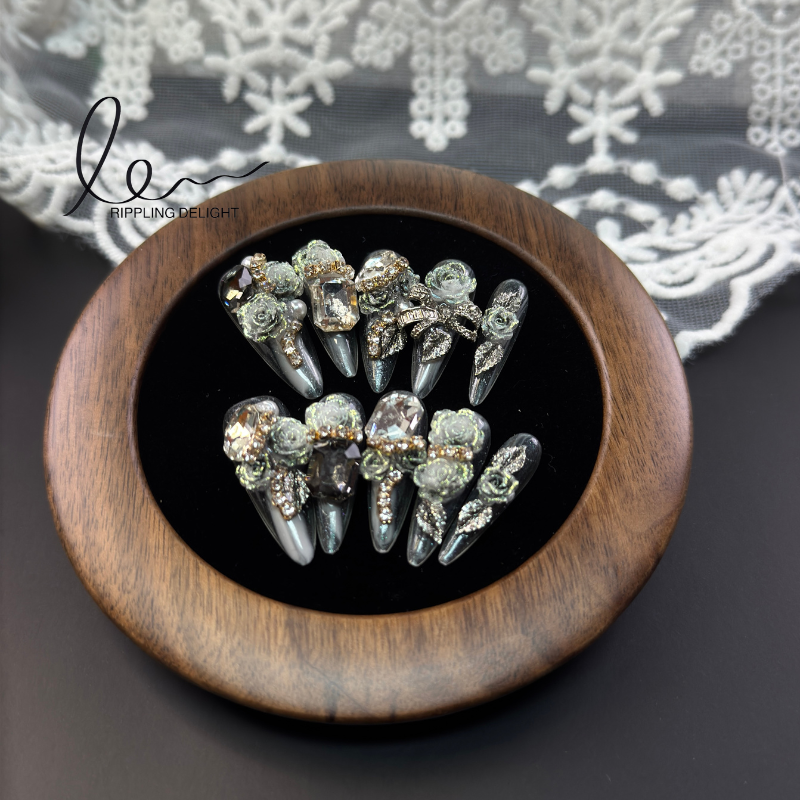 （Long round press-on nails.）Handmade press - on nails featuring black gradation, rhinestone inlays, and floral decorations.