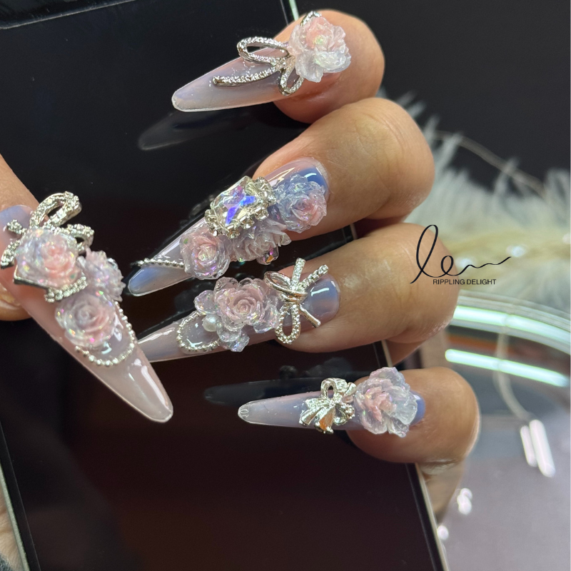 Handmade nail tips feature lifelike pink flowers, encircled by sparkling rhinestones and silver chains.